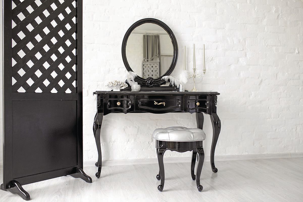 Black boudoir table in a bright room with a white brick wall.